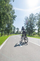 Fototapeta premium Rear view of Caucasian woman riding bike in park. Vertical photo. 
