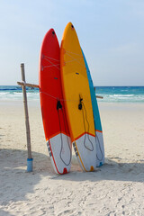 Vibrant paddle boards lean against a wooden support on a sandy beach, ready for watersports...