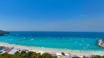 Tourists enjoying parasailing and speedboats in beautiful turquoise ocean water at a tropical island beach resort