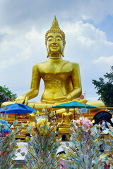 Obraz premium Golden buddha statue radiating serenity amidst colorful offerings in a thai temple, embodying spiritual devotion and cultural heritage