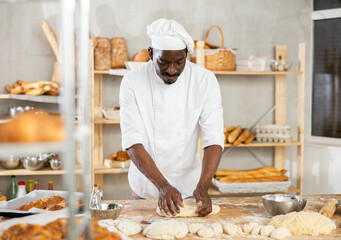 Process of making baguette, loaf or bread in bakery - male baker kneads and rolls dough to give the...