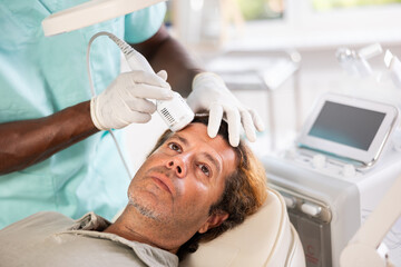Fototapeta premium Adult man undergoing hardware facial treatment using cold hammer helping to shrink pores, repair damaged skin and relieve inflammation in modern cosmetology clinic. Male grooming concept