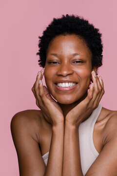 woman touching her face and smiling on pink background