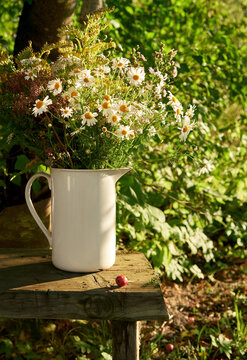 A white pitcher with wildflowers on a rustic wooden table outdoors
