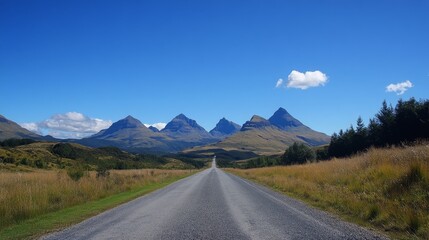 Fototapeta premium 20.A straight road leading into a distant range of towering mountains, with the landscape shifting from rolling hills to rugged peaks. The sky is a deep blue, with a few clouds scattered across it,
