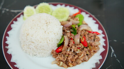 Delicious plate of Thai basil stir-fried minced pork served with steamed rice and garnished with fresh cucumbers.