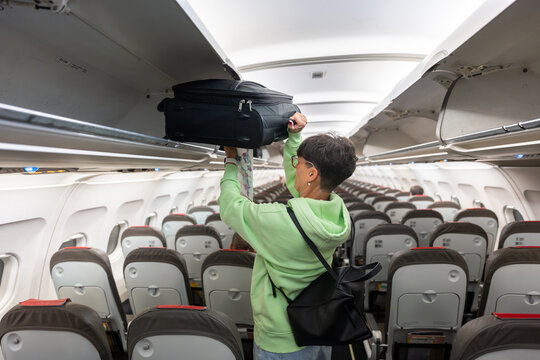 Woman placing luggage in overhead compartment on airplane