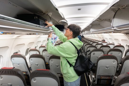 Woman placing luggage in overhead compartment on airplane
