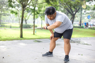 Fat Man In Sportwear Looking Smartwatch While Take a Break During Jogging In Park