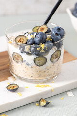 Healthy blueberry Lemon Overnight Oats topped with blueberries, lemon zest and coconut shavings on a light blue wooden counter. Concept for healthy eating and nutrition.