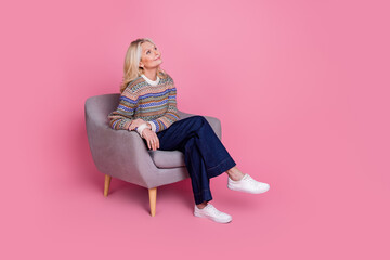 Full size photo of pretty aged lady sit chair look empty space wear pullover isolated on pink color background