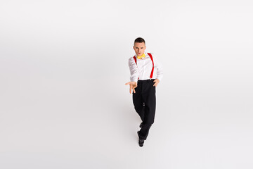 Young man in elegant attire dances with energy and style on a white background