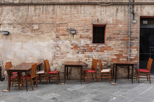 Fototapeta wooden tables and chairs on a street in siena in italy