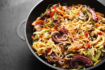 Stir-fry noodles with sea food and vegetables in wok on dark textured table, closeup