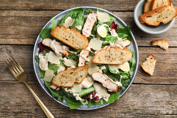 Tasty Caesar salad with chicken served on wooden table, flat lay