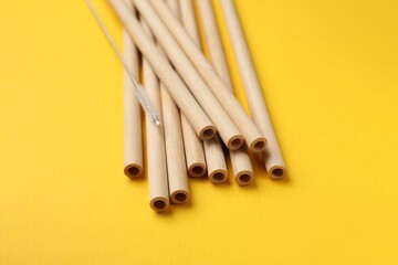 Bamboo drinking straws and cleaning brush on yellow background, closeup