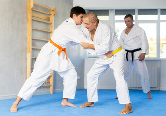 Determined motivated aged man working on martial arts techniques and maneuvers in training fight...