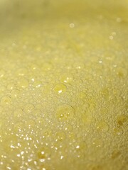Close-up of yellow liquid with numerous tiny bubbles forming a textured, foamy surface, illuminated by soft light, selective focus.