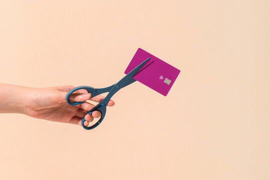 Person Cutting Credit Card With Scissors Against Beige Background