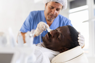 Fototapeta premium Adult African American undergoing high frequency ultrasound therapy to reduce fine wrinkles and rejuvenate facial skin by stimulating collagen production. Modern cosmetology and male grooming concept