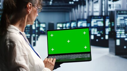 Aged technician in servers center housing high end processors capable of quickly and efficiently performing complex computations and data analysis, using mockup laptop to mend glitches