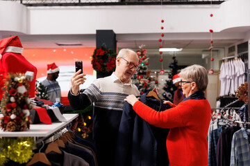 Older clients on video call in store, showing merchandise on online internet chat to buy perfect christmas present for nephew. Two persons using videoconference in shopping mall, festive ornaments.