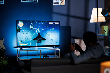 Focused person playing space shooting video games at night, engaging in online multiplayer...