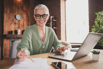 Charming elderly woman enjoying leisure time at home, working on her laptop, embodying modern...