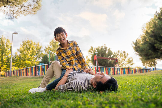 Child laughing while sitting on parent lying in the park