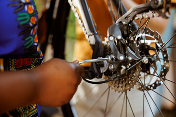 Obraz premium African american female hand using equipment to repair damaged bicycle chain ring outdoors. Closeup of person adjusting bike derailleur with professional tool in home yard.