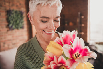 Elderly woman enjoying colorful flowers at home in cozy living room, embracing leisure and warmth