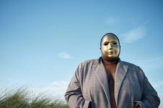 Gold-masked figure stands against sky