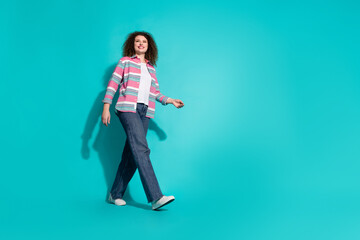 Photo of curly charming young brunette walking lady in striped shirt and jeans interested looking mockup isolated on aquamarine color background