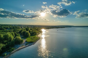 Fototapeta premium Aerial view of a serene lake at sunset, with lush green trees lining the shore and a bright sun shining through the clouds.