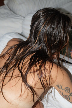A woman with wet hair relaxes on a bed
