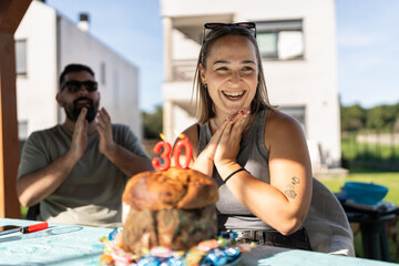 Woman celebrating 30th birthday with friends outdoors, making a wish