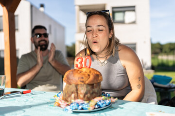 Woman blowing out candles on 30th birthday cake while man claps