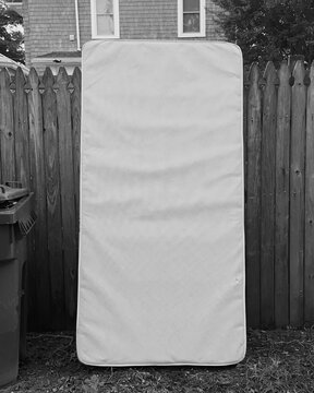 Old bed mattress leaning on a wooden fence