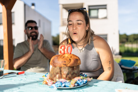 Woman blowing out candles on 30th birthday cake while man claps