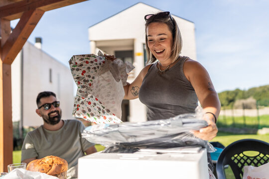 Excited woman unwrapping birthday gift at outdoor party with friends