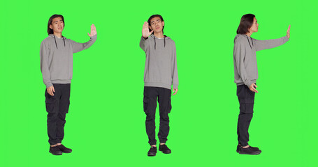 Obraz premium Person showing stop sign with palm raised in studio with greenscreen backdrop, advertising negativity and rejection on camera. Unhappy displeased man doing no gesture, disagreeing.