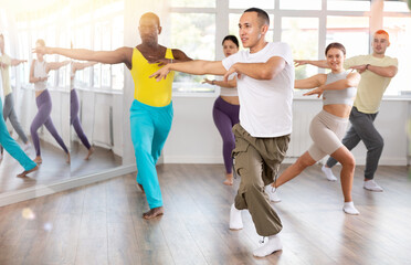 Fototapeta premium During dance workshop, European guy with team of like-minded multinational people learn to perform elements of energy waacking dance. Studio school for amateur and professional dancers