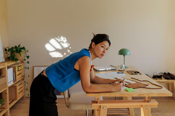 Thoughtful designer leaning on desk and drawing sketches