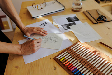 Artist drawing leaves on branch with colored pencils on desk
