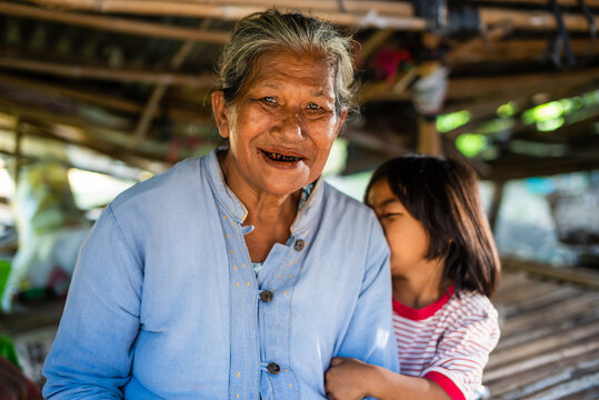 Elderly Thai Woman Smiling with Shy Granddaughter in Rural Setting