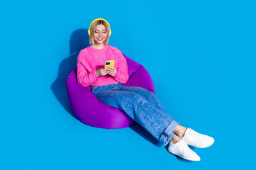 Full body portrait of nice young woman beanbag headphones smart phone wear sweater isolated on blue...