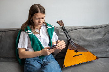 Woman scrolls smartphone on sofa search for balalaika sheet music and chords for song practice....