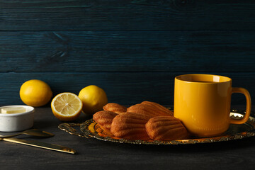 Madeleine cakes, cup, cutlery, butter and lemon on blue wooden background