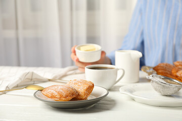 Madeleine cakes, cup of coffee, milk and butter in hand on light background