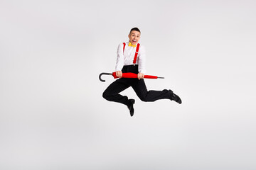 Joyful young man dancing in retro style with vintage umbrella on white background, exuding...